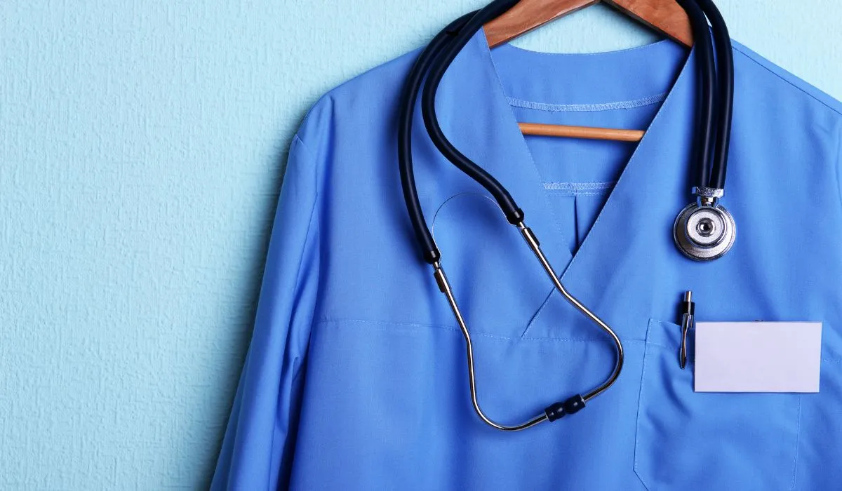 Uniforme de médico con estetoscopio colgado en una pared azul.