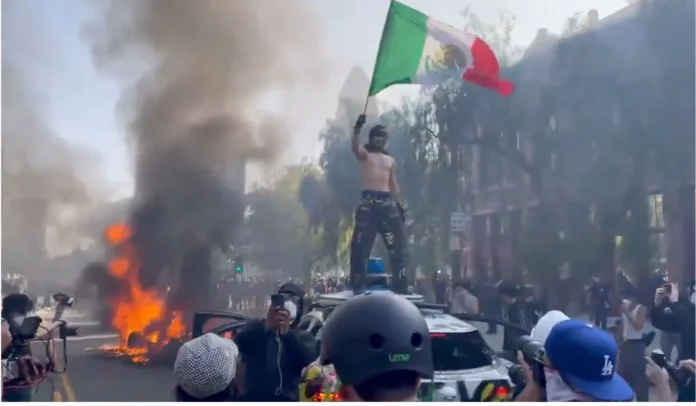 Un manifestante se para sobre un coche Waymo en llamas el 8 de junio de 2025, en el centro de Los Ángeles